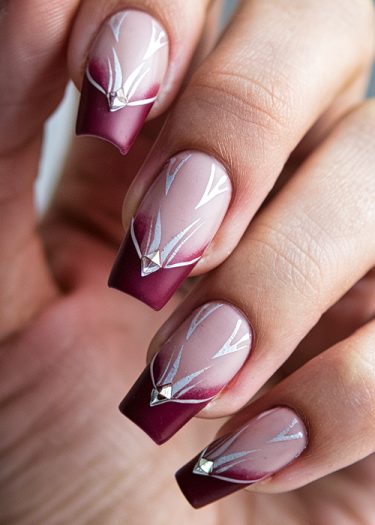 Elegant burgundy-tipped nails with rhinestones and geometric art on a soft pink base.