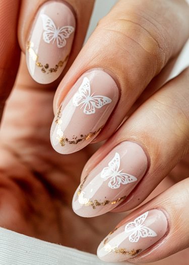 Elegant almond-shaped nails with white butterfly designs and gold glitter accents on a nude pink base.