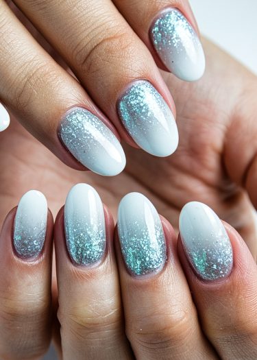 Stunning gradient teal and white almond-shaped nail art with glitter for an elegant look.