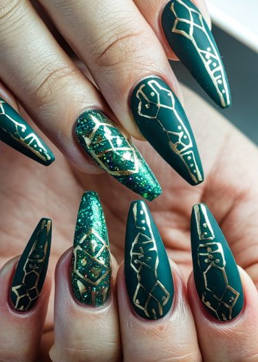 Elegant emerald green stiletto nails with gold geometric designs and glittery accents.