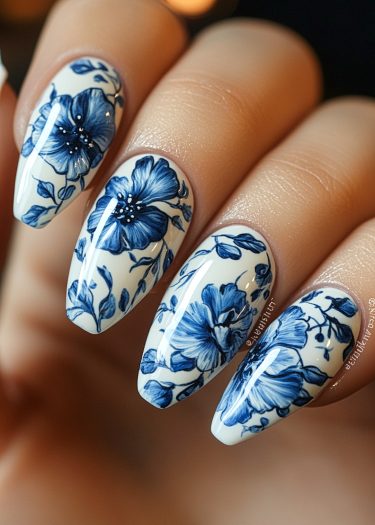 Elegant almond-shaped nails featuring intricate blue floral designs on a white base.