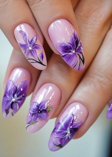 Elegant floral nail art featuring almond-shaped nails in pink with vibrant purple designs.