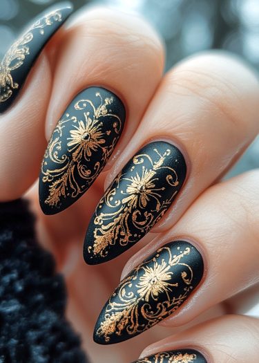 Exquisite black stiletto nails with ornate gold floral designs for elegant nail art inspiration.