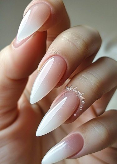 Elegant stiletto nails with ombre nude pink and white gradient, adorned with sparkles.