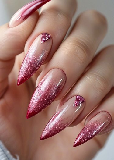 Elegant stiletto nails featuring a pink to red gradient with rhinestone accents for a glamorous look.