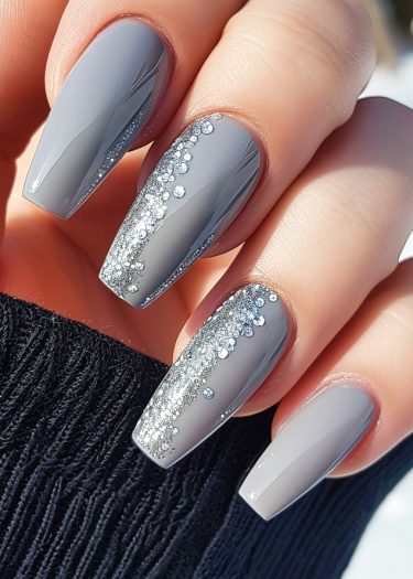 Elegant gray almond-shaped nails with glitter accents on a stylish black fabric background.