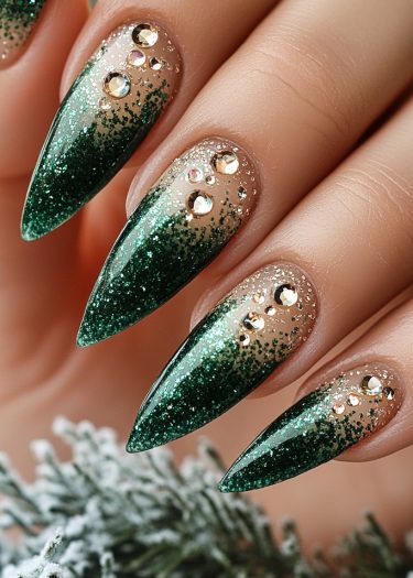 Elegant stiletto nails with green glitter and rhinestones for a luxurious, festive look.