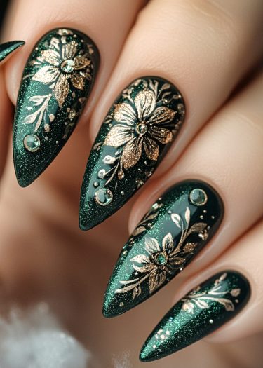 Stunning emerald green stiletto nails with intricate gold floral designs and sparkling rhinestones.