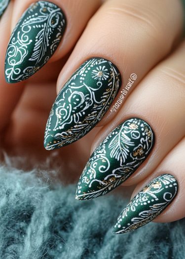 Elegant emerald green nail art featuring intricate white and gold designs on almond-shaped nails.