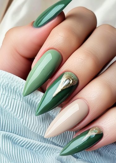 Elegant green stiletto nails with gold accents on textured fabric background for stylish nail art.