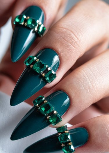 Elegant emerald green stiletto nails adorned with sparkling gems for a luxurious manicure look.