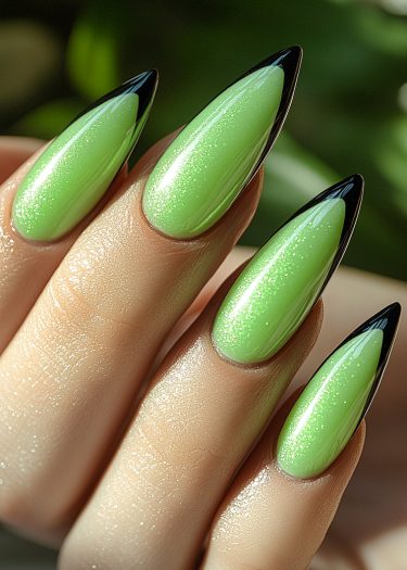 Elegant lime green stiletto nails with black tips against a natural background.