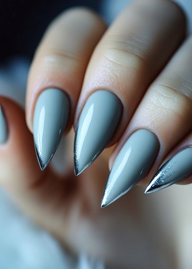 Sleek matte gray stiletto nails with metallic silver accents in an elegant manicure design.