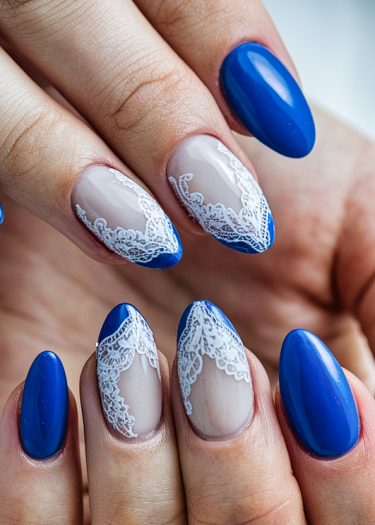 Elegant almond-shaped blue nails with intricate white lace designs for a stunning manicure.