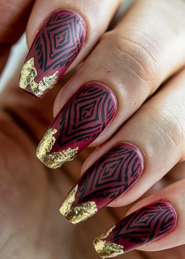 Elegant burgundy nails with geometric black patterns and gold leaf accents for a sophisticated look.