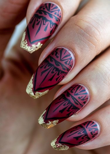 Elegant maroon nail art featuring geometric patterns and luxurious gold leaf accents.