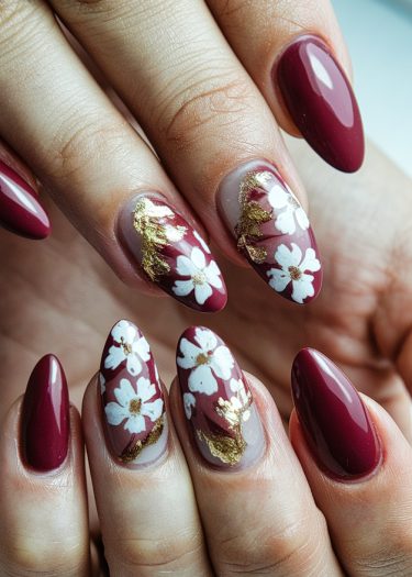 Sophisticated burgundy nail art featuring floral designs and gold accents for a luxurious look.