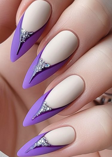 Elegant almond-shaped matte beige nails with vibrant violet tips and sparkling rhinestones.