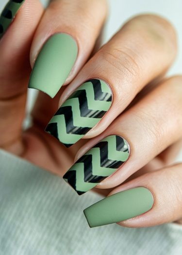 Elegant matte green nails with glossy black zigzag designs showcase intricate nail art.