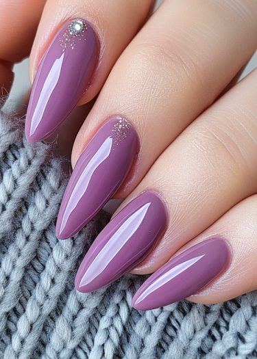 Elegant mauve nails with rhinestones resting on soft gray fabric, showcasing modern nail art.