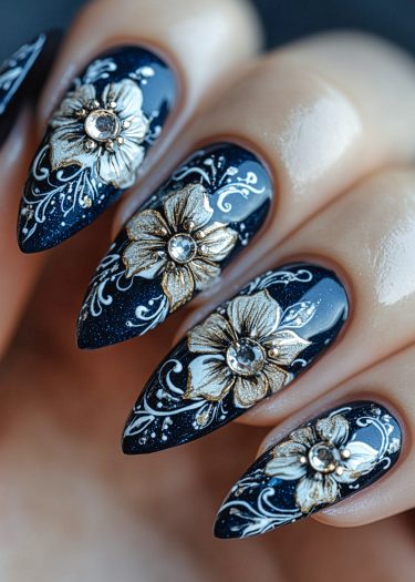 Stunning black almond-shaped nails with gold floral designs and rhinestones for a chic manicure.