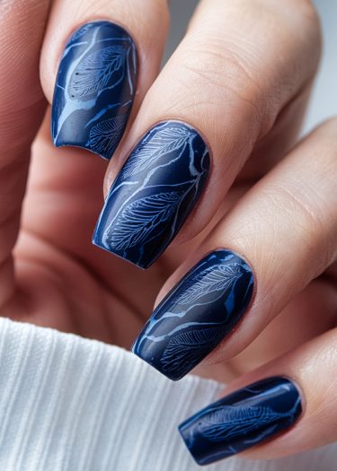 Elegant navy blue nail art featuring intricate silver leaf designs for a sophisticated look.