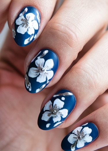 Elegant navy blue nail art with intricate white floral designs and silver accents.