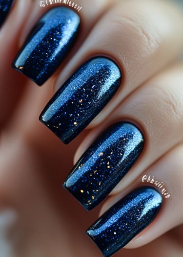 Stunning deep blue nails with glitter, showcasing elegant nail art and glossy finish.