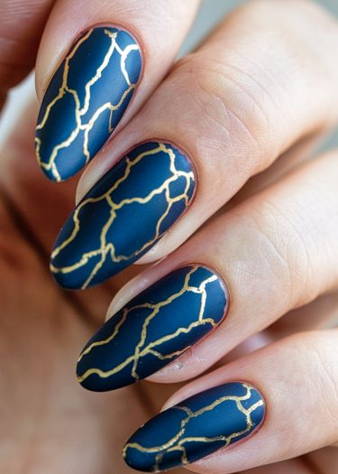 Elegant navy blue and gold nail art with intricate designs on almond-shaped nails.