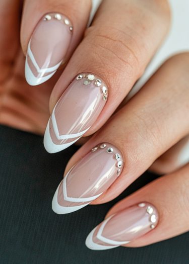 Elegant nude almond nails with geometric white lines and silver embellishments for a chic manicure.