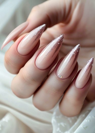 Elegant nude stiletto nails with glitter ombre and rhinestone accents for sophisticated nail art.