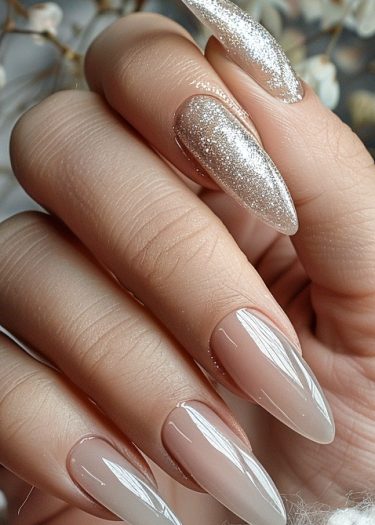 Sleek almond-shaped nude ombre nails with a glittery gold accent for elegant manicure style.