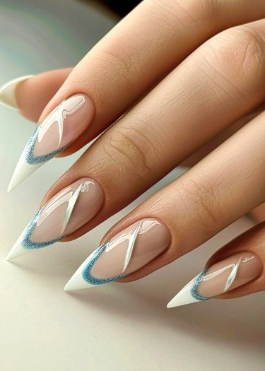 Elegant nude stiletto nails with intricate white and blue glitter designs.