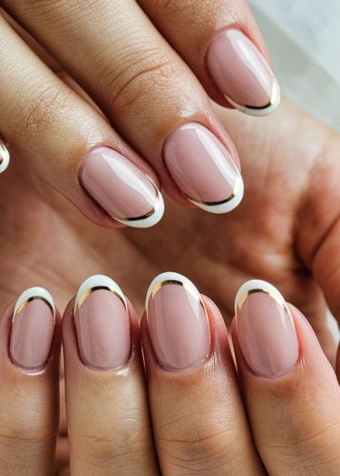 Elegant nude pink manicure featuring French tips with gold accents for a sophisticated look.