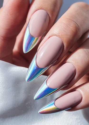 Elegant stiletto nails with holographic tips over a nude base on satin background.