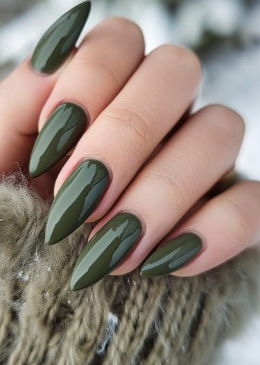 Elegant olive green stiletto nails on a smooth hand resting on soft knit fabric.