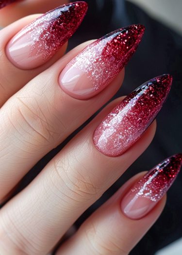 Elegant stiletto nails with red ombre and glitter for a glamorous manicure look.