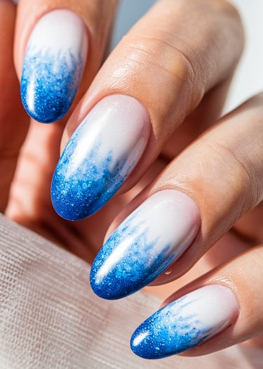 Elegant almond-shaped ombré nails in white and blue with glittery tips for a chic look.