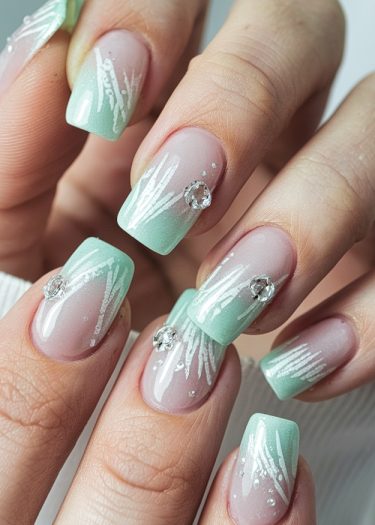 Elegant ombre nail art featuring mint green tips, white patterns, and sparkling rhinestones.