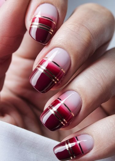 Elegant ombré nail art with gold accents in deep red and pink hues.