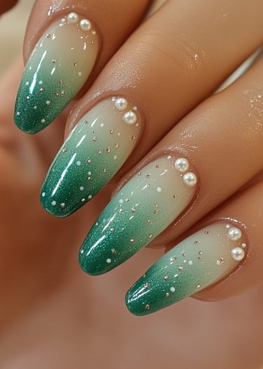 Elegant ombre nails with emerald green tips, detailed with pearls and gold embellishments.