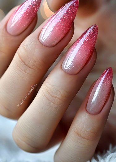 Elegant stiletto nails with pink ombré and glitter shine in a close-up photo.