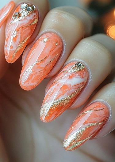 Elegant coral orange almond-shaped marble nails with gold accents and rhinestones for a chic look.