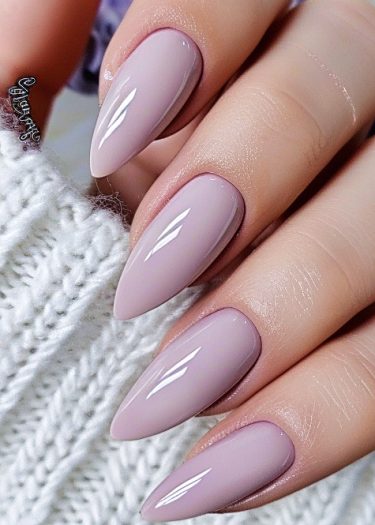 Elegant stiletto nails in pale mauve polish against a cozy knitted background.