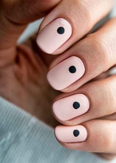 Chic pastel pink nails with a minimalist black dot design for elegant nail art.