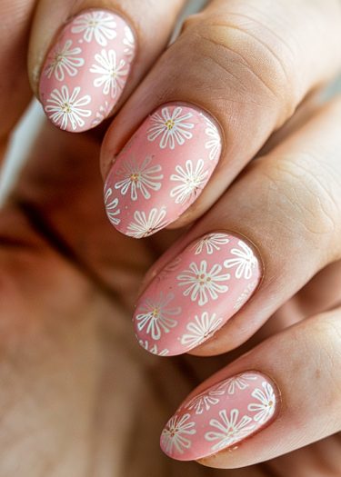 Elegant pink nails with daisy designs showcase intricate floral art and stylish almond shape.