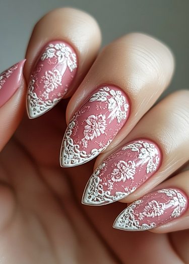 Elegant pink stiletto nails with intricate white lace designs for a sophisticated nail art look.