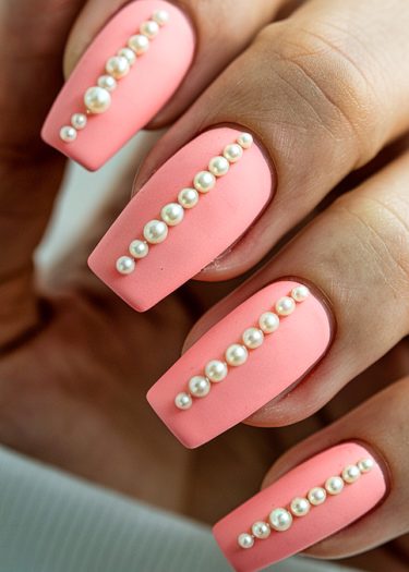 Elegant pink matte nails adorned with pearls in a chic coffin style.