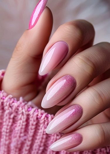 Elegant pink ombre nails with glitter against a cozy textured background.