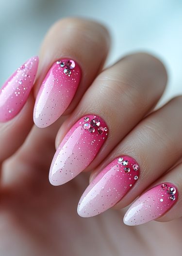 Elegant pink ombre nails with glitter and rhinestones, showcasing a chic almond shape.